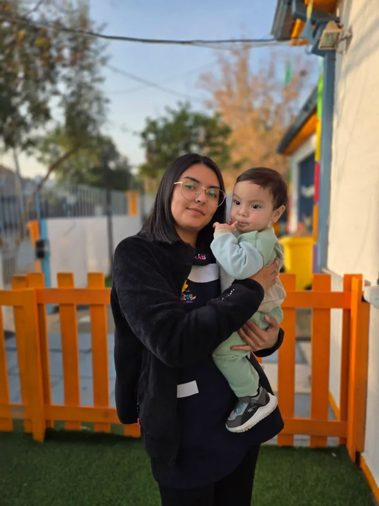 Cuidadora sosteniendo a un bebé en área exterior protegida del jardín infantil