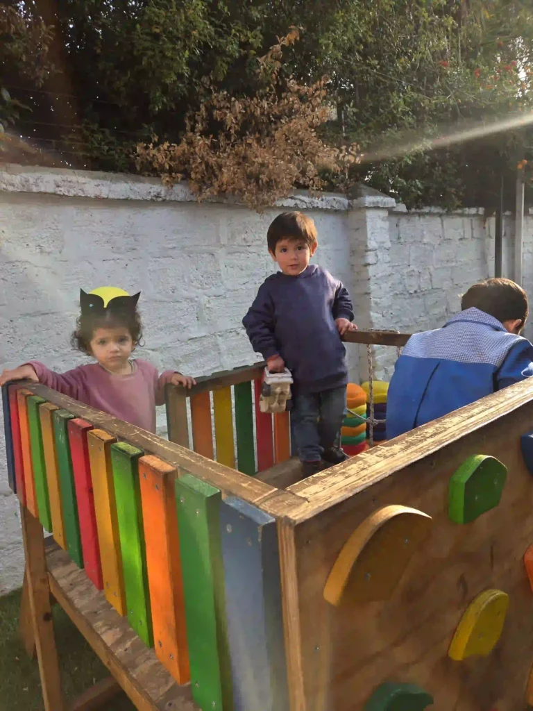 Niños explorando estructura de madera en patio seguro de jardín infantil